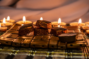 Sweets, milk candies and dark chocolate broken, on the background of lights, candles. Warm, soft and pleasant shade. Dessert is gentle and natural in a romantic home environment.