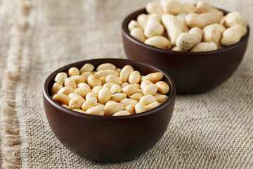 Peanuts in the shell and peeled close-up in cups. Roasted peanuts in their shells and peeled against a brown cloth.