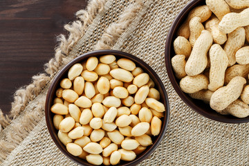 Peanuts in the shell and peeled close-up in cups. Roasted peanuts in their shells and peeled against a brown cloth.