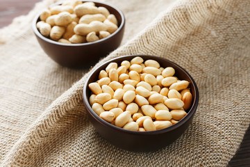 Peanuts in the shell and peeled close-up in cups. Roasted peanuts in their shells and peeled against a brown cloth.