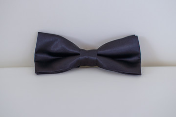 Silky bow tie in dark blue or navy solid color positioned on a white leather cushion with white background, elegant accessory for formal attire