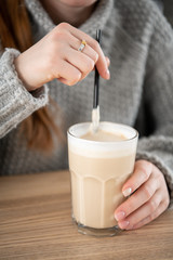 Woman's hand holding a glass cup with coffee. Woman sitting at cafe, selective focus on a cup. Cozy morning concept.