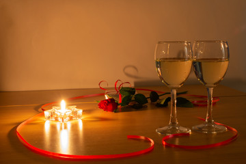 Two glasses with white wine , a candle, a rose and a red ribbon. Meeting