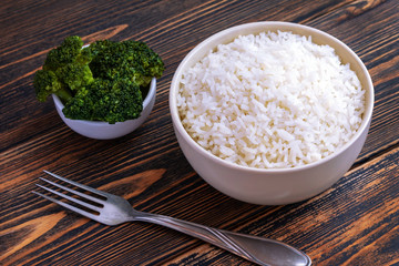 A Cup of white Rice and broccoli on a dark wooden background. Dietary or vegetarian food.