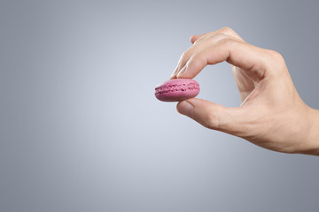 Hand holding a pink macaroon on grey background