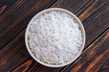 A Cup of white rice on a dark wooden background. Dietary or vegetarian food. Top view. Food cooked at home.