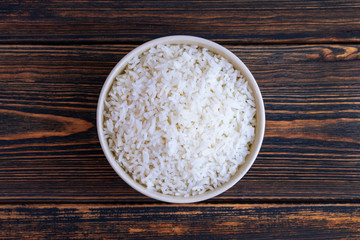 A Cup of white rice on a dark wooden background. Dietary or vegetarian food. Top view. Food cooked at home.