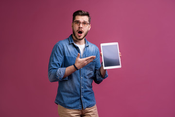 Happy attractive young man standing and using tablet over pink background.