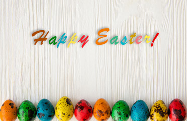 Happy Easter. Colored, boiled, quail eggs on a white wooden background with colored letters.
