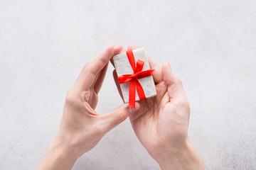 Hands holding little gift with red bow