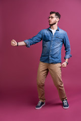 Fototapeta premium Funny man in casual is having some fun. He is posing and dancing. Isolated on pink background.