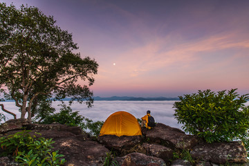 The traveler and orange tent on high mountain and sea of mist.