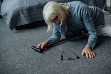 lonely senior woman lying on floor with walking stick and feeling unwell at home