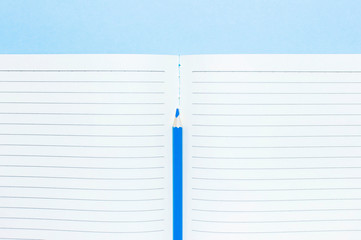 Color pencils and clean notebook in line on blue background top view flat lay copy space. Wooden...
