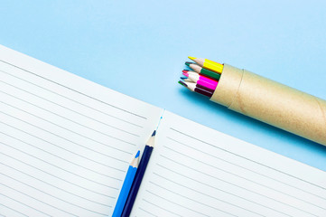 Color pencils and clean notebook in line on blue background top view flat lay copy space. Wooden...