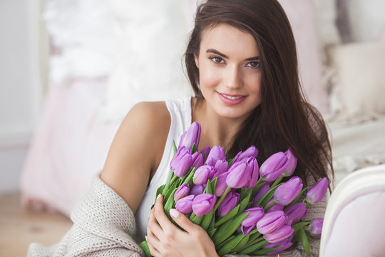 Close up portrait of young beautiful woman indoors. Attractive woman with flowers. Female with tulips. Spring bouquet.