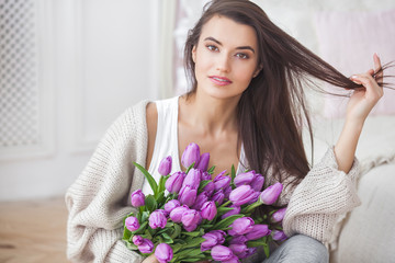Close up portrait of young beautiful woman indoors. Attractive woman with flowers. Female with tulips. Spring bouquet.
