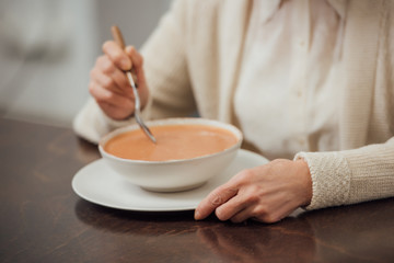 cropped view of senior woman sitting at table and eating cream soup at home