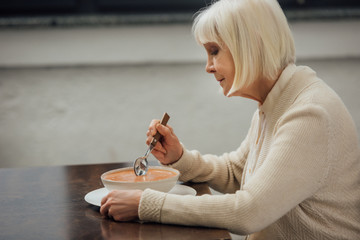 sad senior woman sitting at table and eating cream soup at home