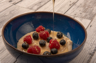 Bowl of porridge with raspberries, blueberries and honey on a wooden background 