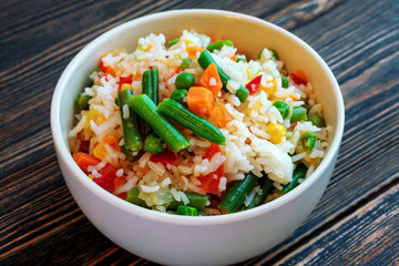 A Cup of white rice with vegetables on a dark wooden background. Prepared without loss of vitamins.