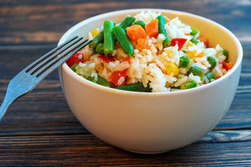 A Cup of white rice with vegetables on a dark wooden background. Prepared without loss of vitamins.