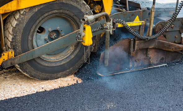 Worker regulate tracked paver laying asphalt heated to temperatures above 160 ° pavement on a runway