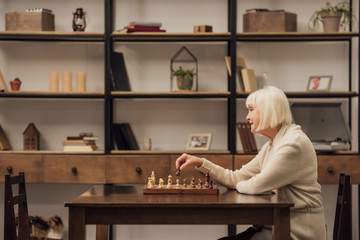 selective focus of senior woman sitting at table and playing chess in living room