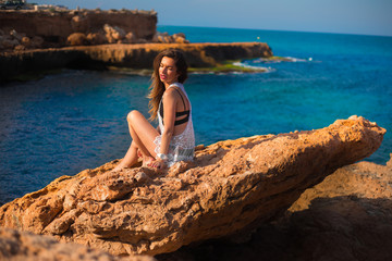 Fototapeta na wymiar Model sitting on edge of rocks with sea view 