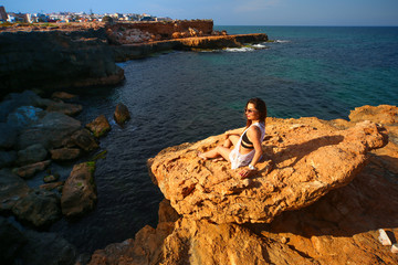 Model sitting on edge of rocks with sea view 