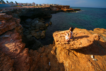 Model sitting on edge of rocks with sea view 