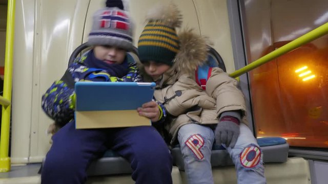 Timelapse shot of two kids in winter clothes using digital tablet when traveling by trolleybus in evening city