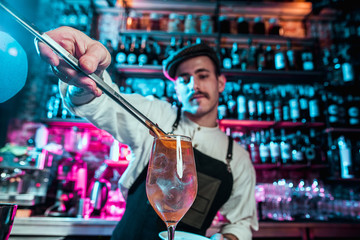 Expert barman is making cocktail at night club or bar. Glass of fiery cocktail on the bar counter against the background of bartenders hands with fire. Barman day concept