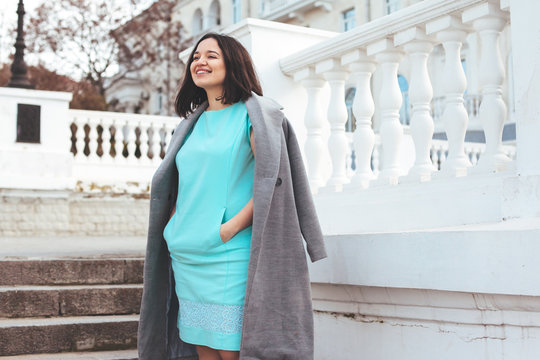 Beautiful model in blue dress and grey coat on city street