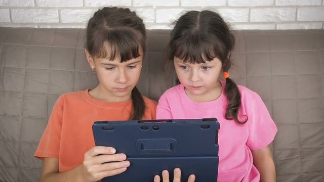 Children with a tablet. Children on the Internet without parental control. Little girls in shock looking at the screen of the gadget.