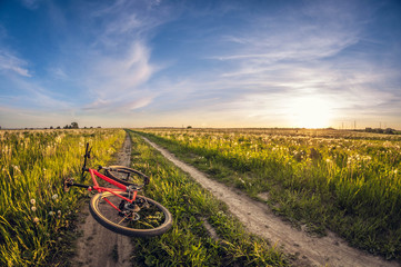 Fototapeta na wymiar bike lying on a dirt road in a field at sunset