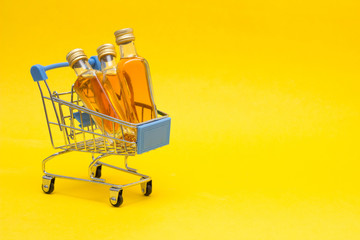 Small bottles of alcohol in a shopping trolley, buying alcohol, yellow background, copy space, sale
