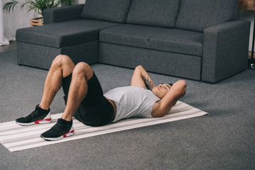 Obraz premium tattooed bi-racial man lying on fitness mat and doing exercise