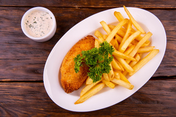 Cutlet chicken in breadcrumbs, is served with French fries and cheese sauce