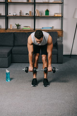 Fototapeta na wymiar strong mixed race man training with dumbbells in living room