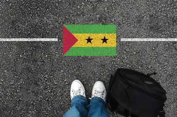  a man with a shoes and backpack is standing on asphalt next to flag of Sao Tome and Principe and...