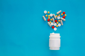 Pills heart out of pill bottle on blue background, top view