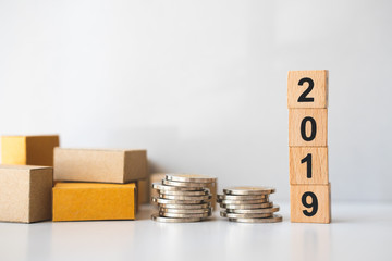 Closeup cardboard boxes with stack coins and wooden block year 2019 using as business and logistics concept
