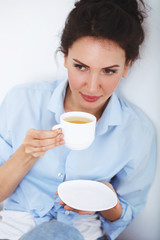 Young beautiful brunette woman, wearing blue shirt, drinking hot tea at home.