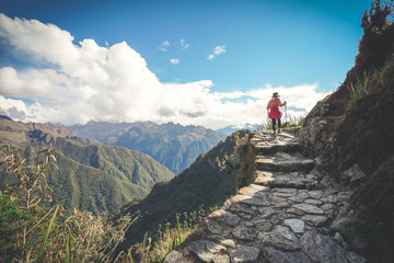 A female hiker is walking on the famous Inca trail of Peru with walking sticks. She is on the way...
