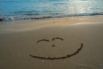 Writing smile on sand beach with blue waves ocean.