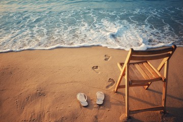 White sandals and wooden chairs placed on the sand with blue waves ocean.