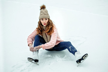 Beautiful girl in warm clothes sitting on ice rink after falling and laughing