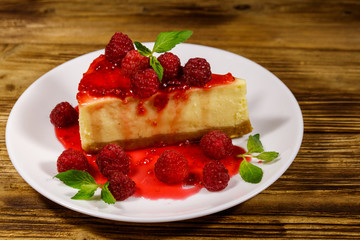 Piece of tasty New York cheesecake with raspberries and raspberry jam in a white plate on wooden table