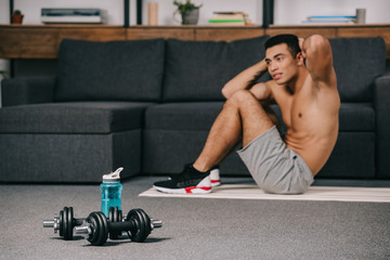 selective focus of dumbbells near sport bottle with bi-racial man on background